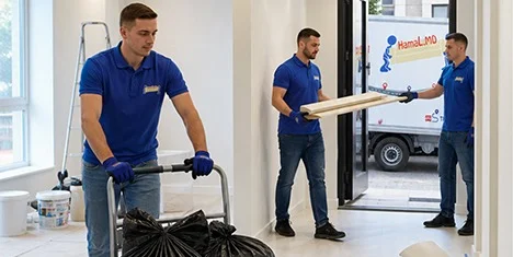 Грузчик HamaL.MD везет мешки со строительным мусором на тележке, а бригада выносит доски к бусу у входа